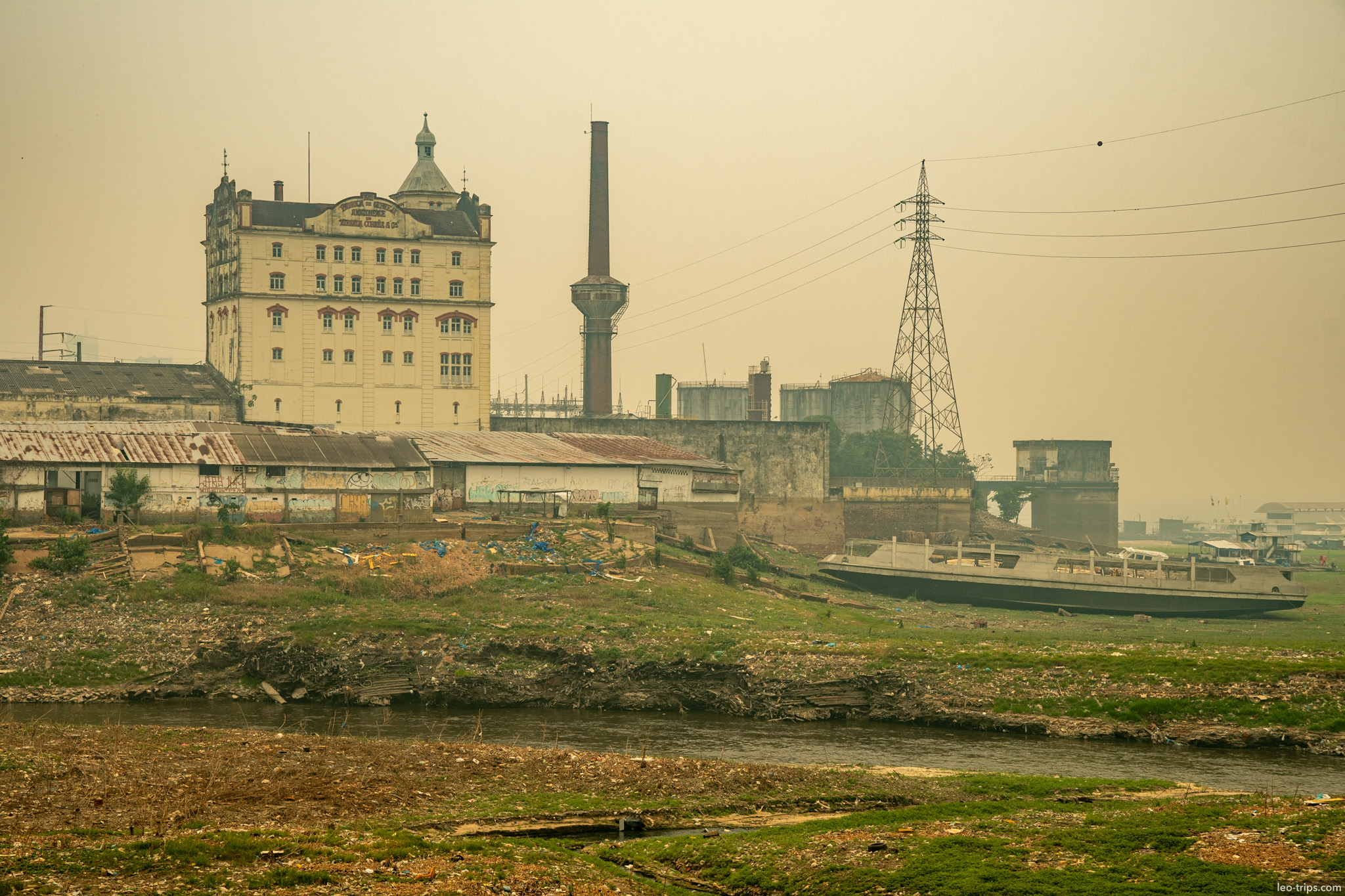 A view of the historic industrial waterfront, featuring an old factory building with a smokestack against a hazy sky