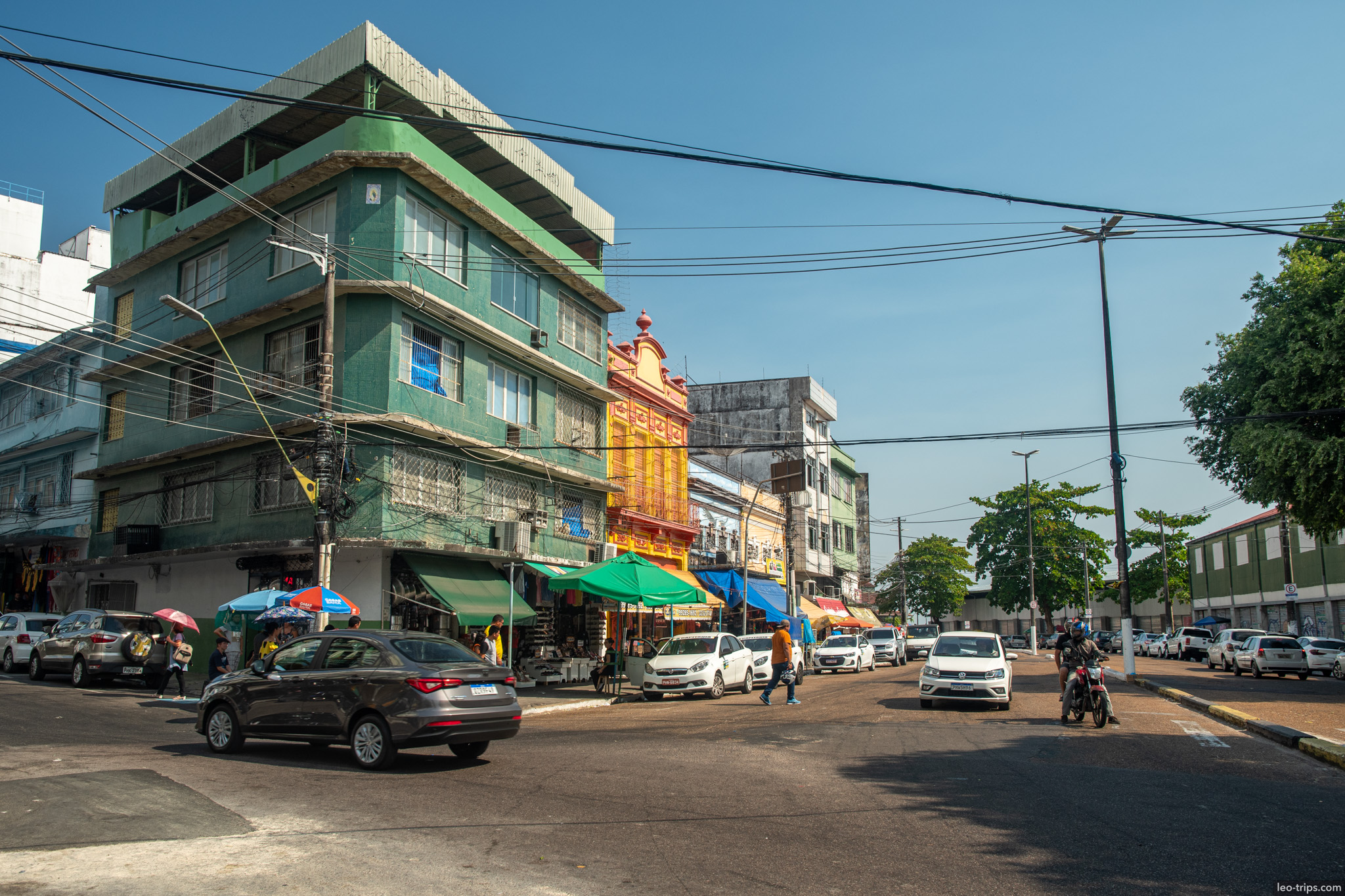 A busy street intersection in downtown Manaus featuring a distinctive green commercial building and daily traffic