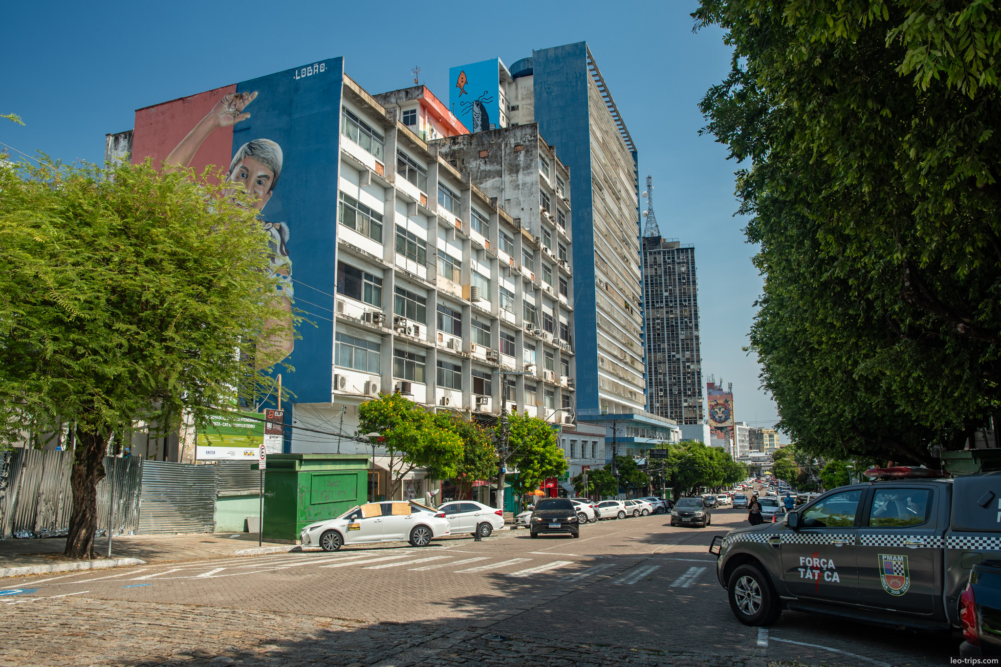 A street scene in Manaus featuring a large, colorful mural on a building facade, highlighting the city's urban art and tropical atmosphere