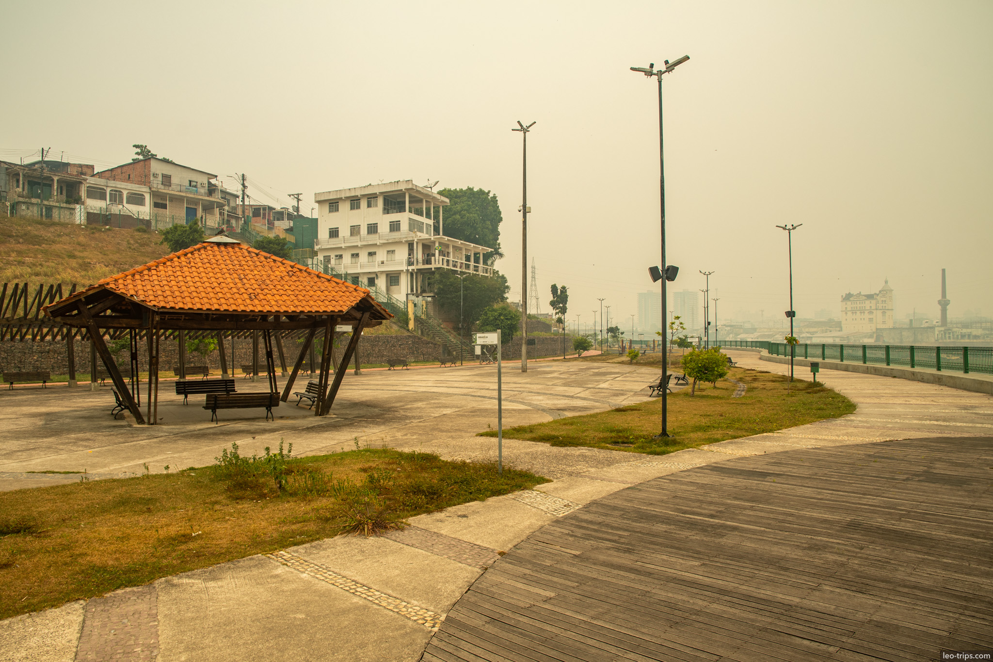 A view of the riverside promenade with a wooden gazebo, looking out towards the hazy horizon during the dry season