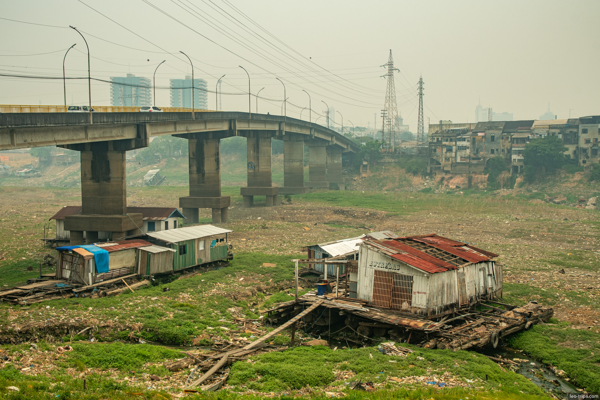 A view of stilt houses (palafitas) along a dried riverbed near a concrete bridge, highlighting the social contrasts of the city