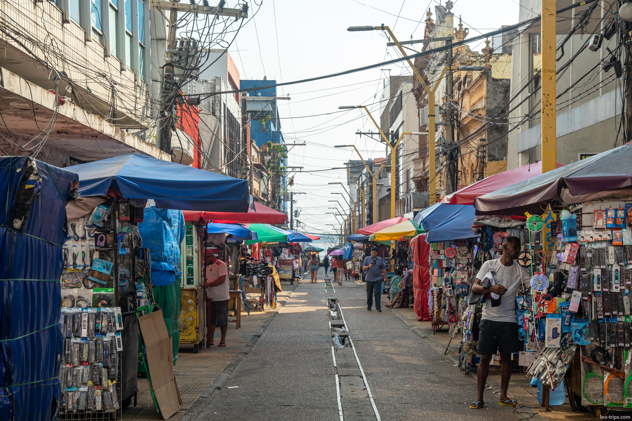 A crowded street market scene filled with blue stalls and vendors selling affordable goods and clothing