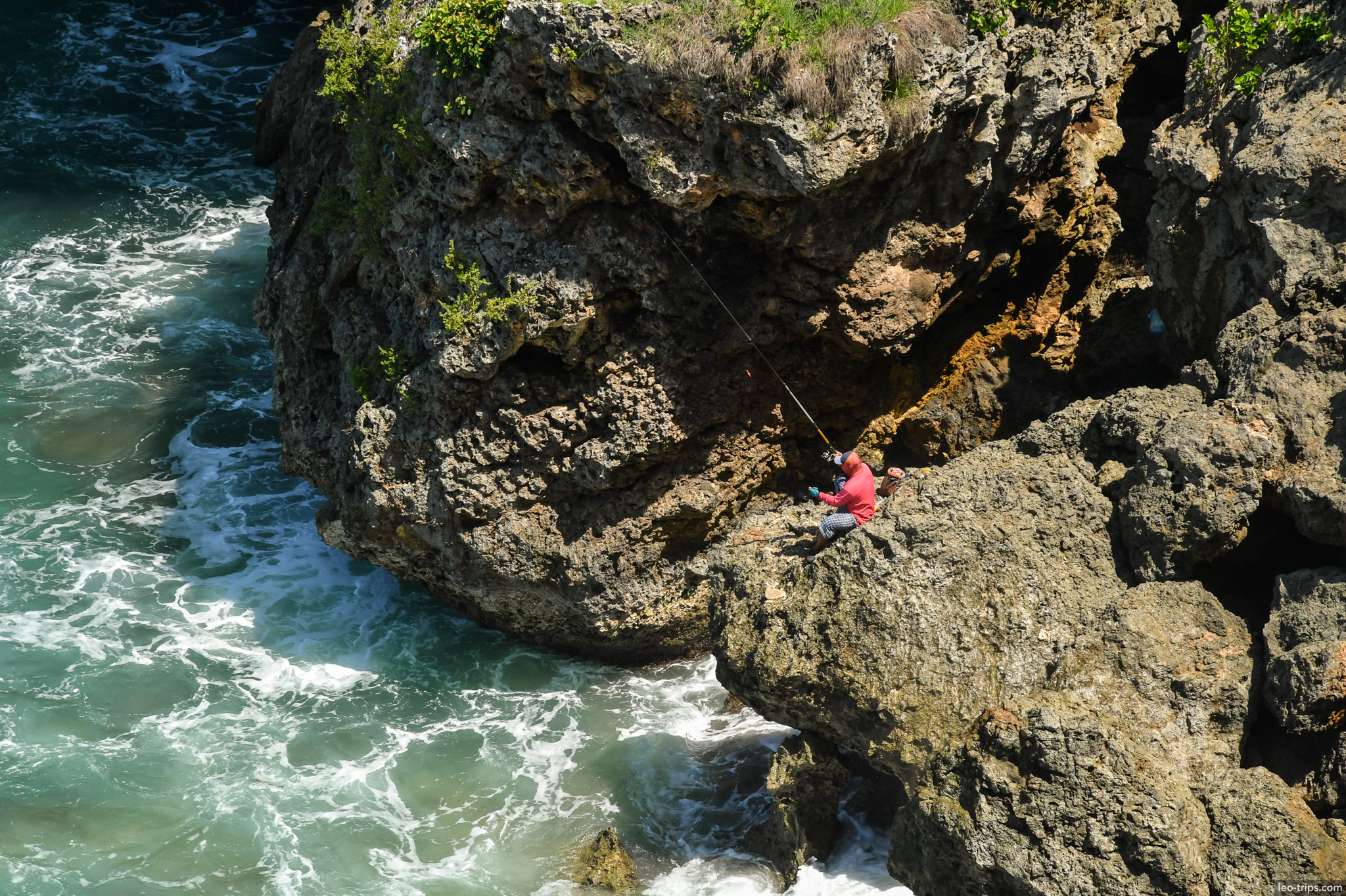 fisherman on rocky cliff above surf bali