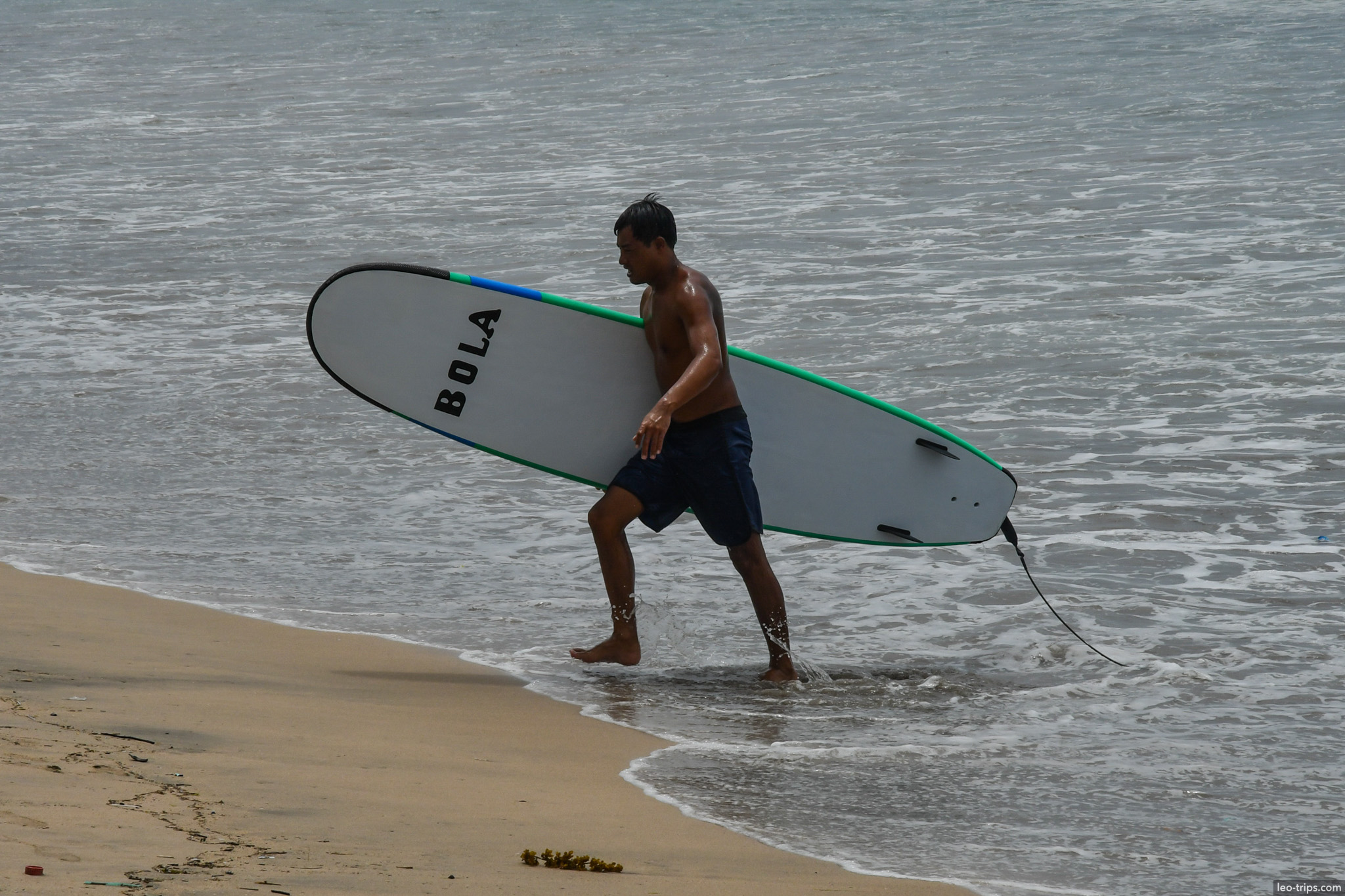 surfer carrying board into waves bali