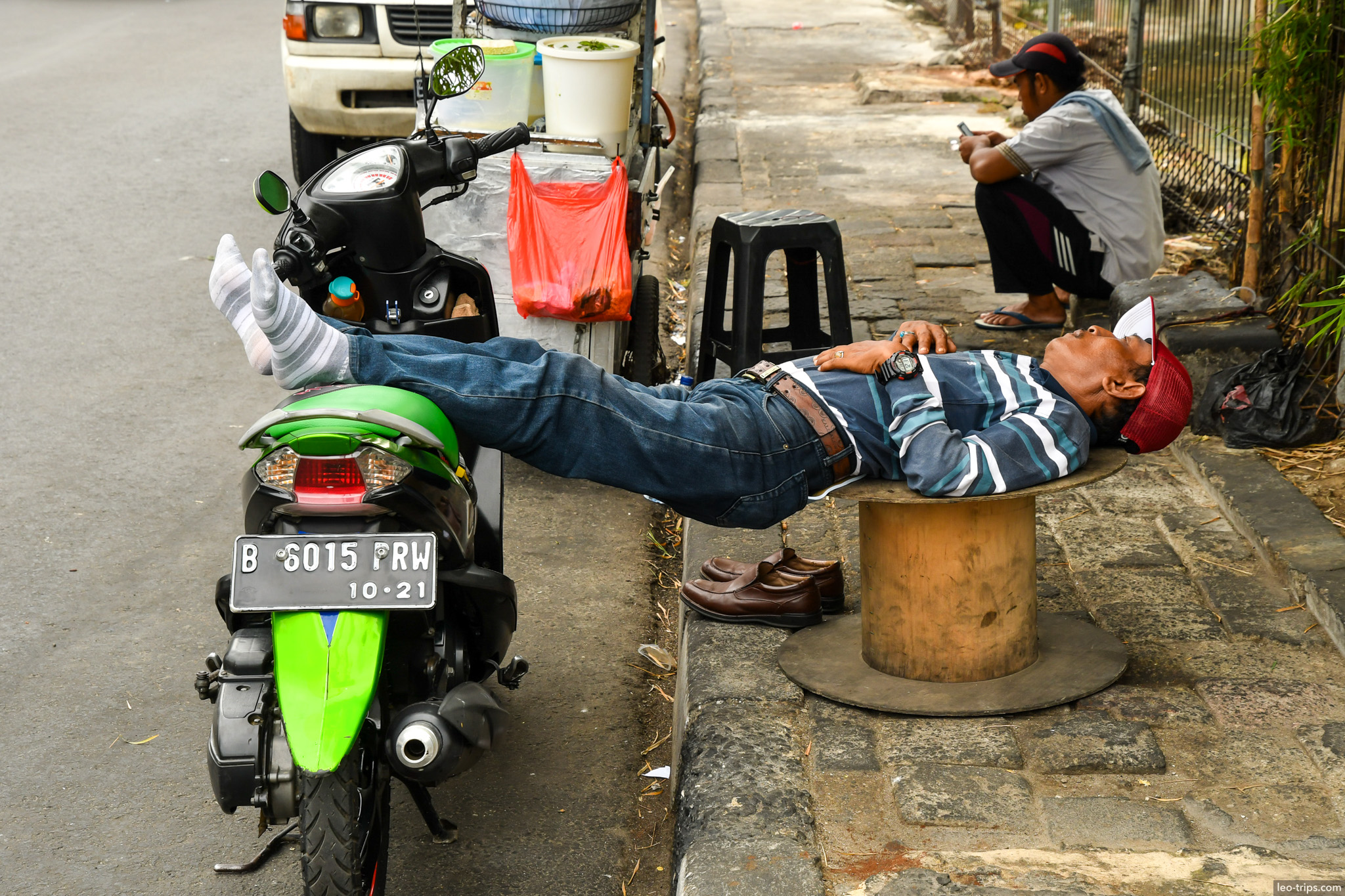 man napping on bollard beside green scooter jakarta jakarta