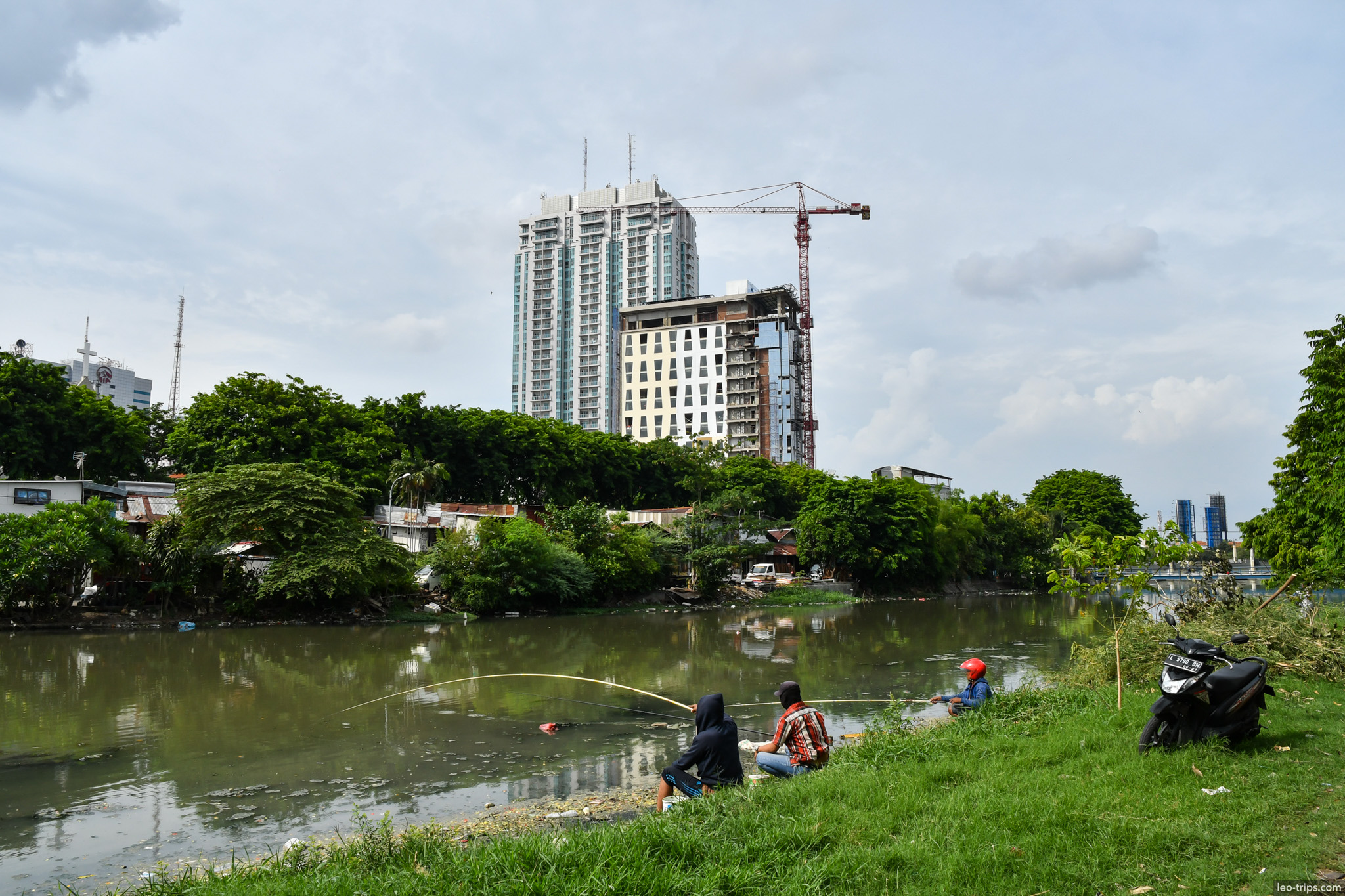 men fishing riverbank skyscraper construction surabaya