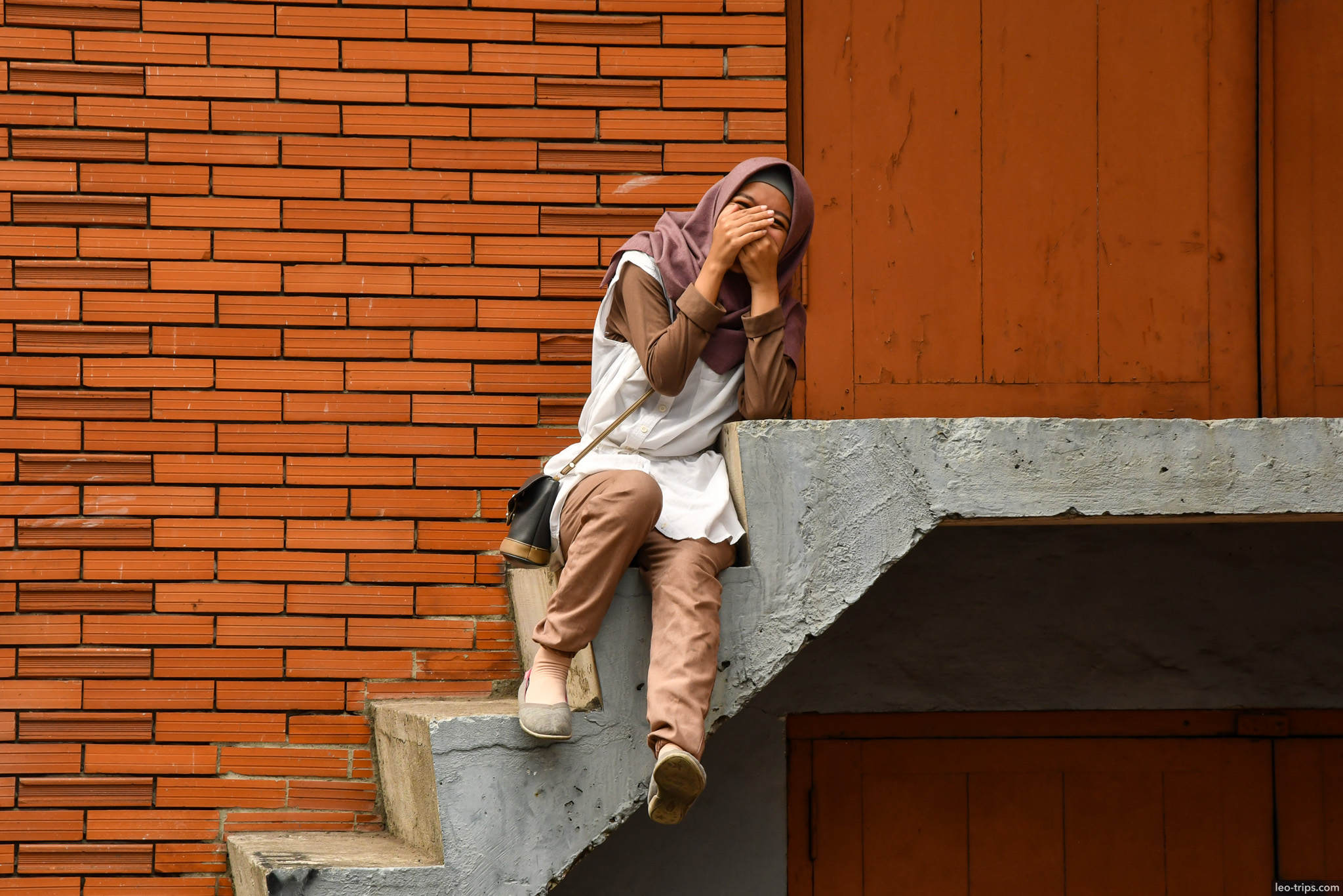 woman in hijab laughing sitting on brick steps surabaya