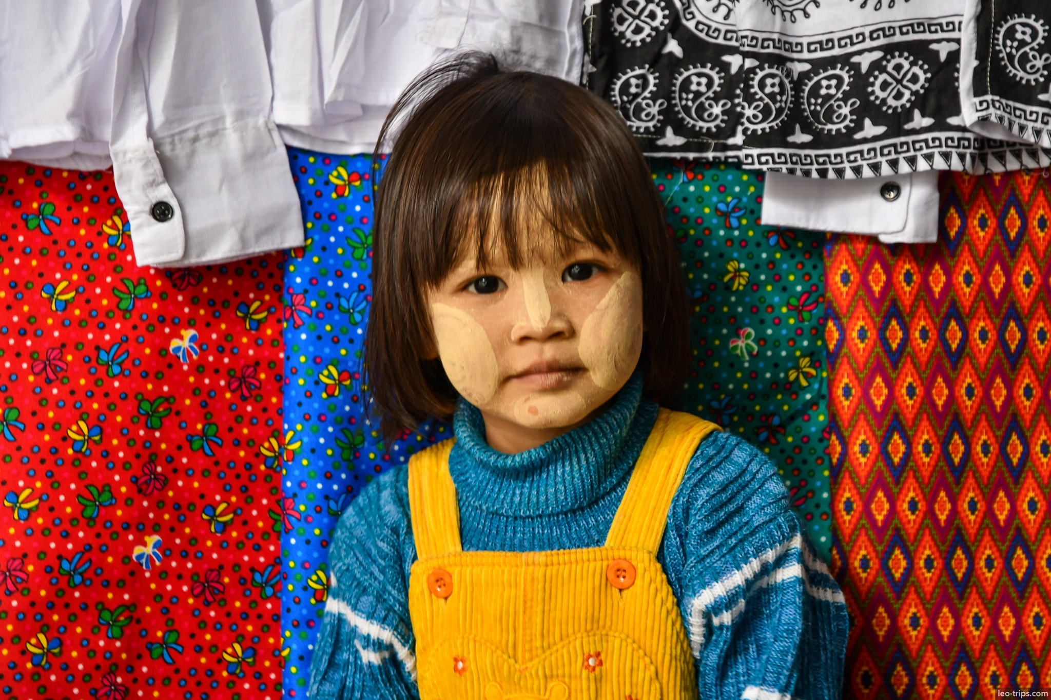 burmese girl with thanaka among colorful fabrics mandalay